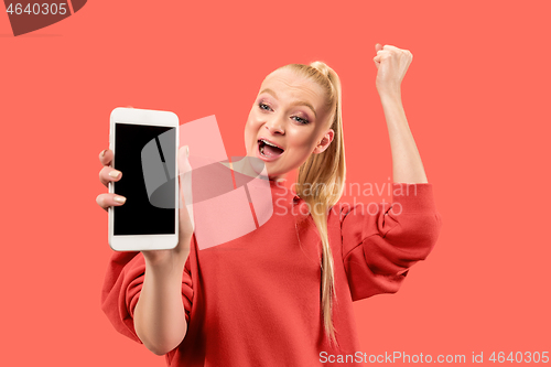 Image of Portrait of a confident casual girl showing blank screen mobile phone isolated over coral background