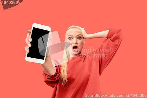 Image of Portrait of a confident casual girl showing blank screen mobile phone isolated over coral background