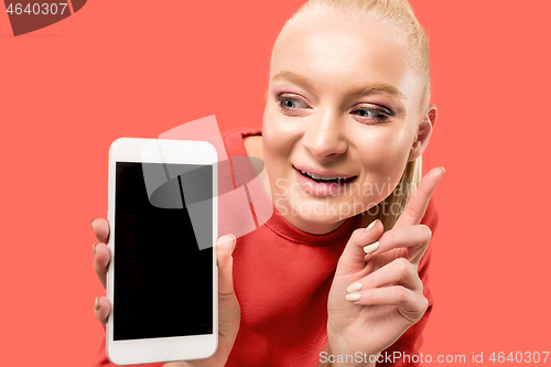 Image of Portrait of a confident casual girl showing blank screen mobile phone isolated over coral background