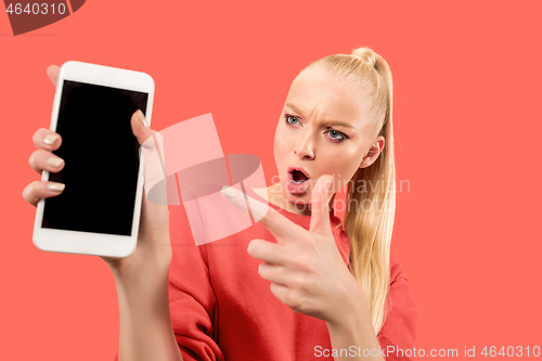 Image of Portrait of a confident casual girl showing blank screen mobile phone isolated over coral background