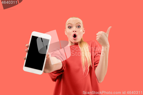 Image of Portrait of a confident casual girl showing blank screen mobile phone isolated over coral background