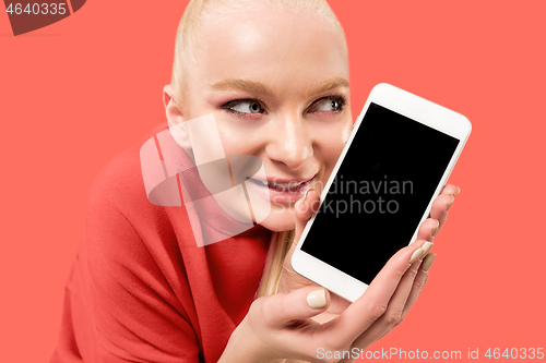 Image of Portrait of a confident casual girl showing blank screen mobile phone isolated over coral background