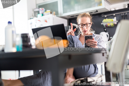 Image of Stay at home and social distancing. Woman in her casual home clothing working remotly from kitchen dining table. Video chatting using social media with friend, family, business clients or partners