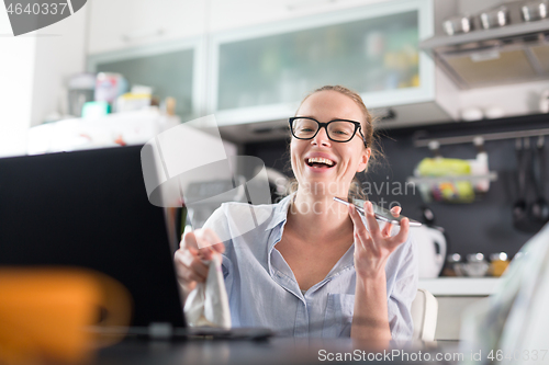 Image of Stay at home and social distancing. Woman in her casual home clothing working remotly from kitchen dining table. Video chatting using social media with friend, family, business clients or partners