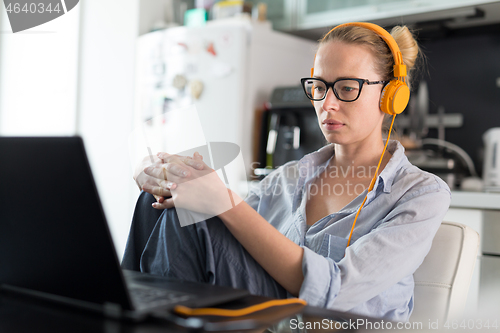 Image of Female freelancer in her casual home clothing working remotly from her dining table in the morning. Home kitchen in the background.