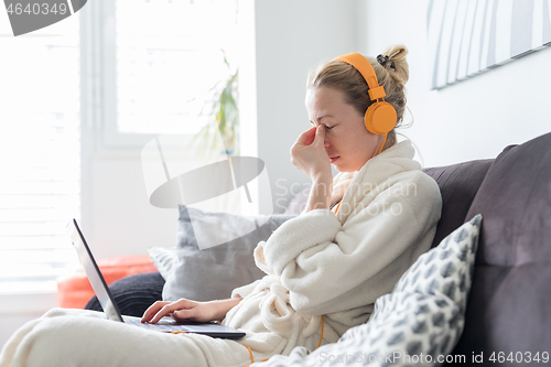 Image of Stressed business woman in her casual home bathrobe working remotly from her living room during corona virus pandemic crisis. Stay at home and social distancing