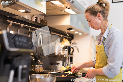 Image of Stay at home housewife woman cooking in kitchen, salting dish in a saucepan, preparing food for family dinner.