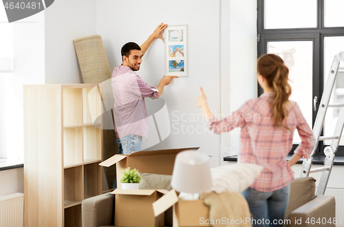 Image of happy couple moving to new home and hanging photo