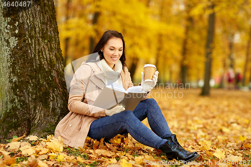 Image of woman reading book with coffee in autumn park