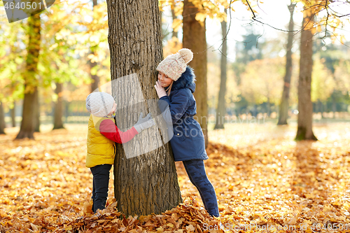 Image of happy children at tree trunk in autumn park