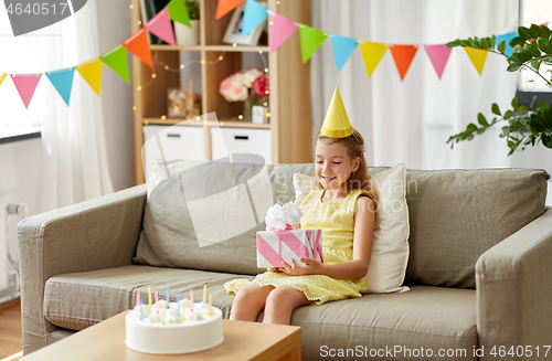 Image of happy girl in party hat with birthday gift at home