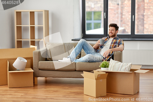 Image of man with boxes and drinking coffee at new home