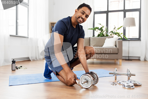 Image of smiling indian man assembling dumbbells at home