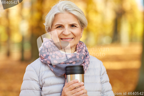 Image of old woman with hot drink in tumbler at autumn park