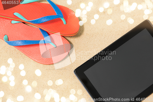 Image of tablet computer and flip flops on beach sand