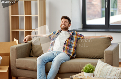 Image of happy man with boxes sitting on sofa at new home