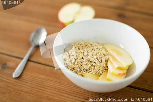 Image of oatmeal in bowl with apple and spoon on table