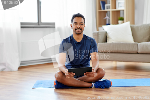 Image of indian man with tablet pc and exercise mat at home