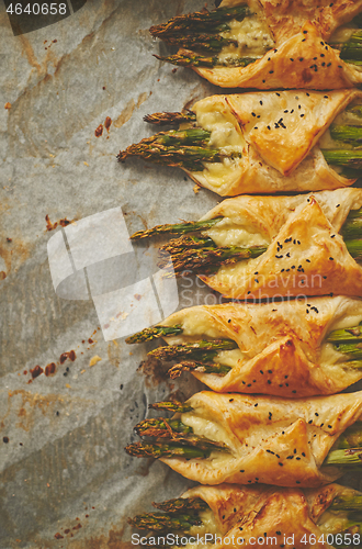 Image of Green asparagus baked with cheese, wrapped in puff pastry. Placed on baking paper with copy space