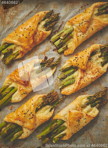 Image of Baked green asparagus in puff pastry sprinkled with sesame seeds. Placed on a white baking paper