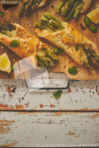 Image of Baked green asparagus wrapped in puff pastry. Served on wooden board. With copy space