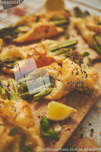 Image of Baked green asparagus wrapped in puff pastry. Served on wooden board. With selective focus