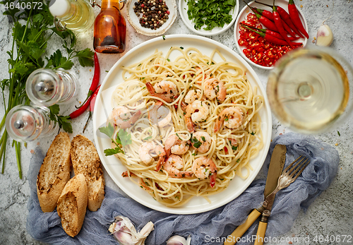 Image of Spaghetti with shrimps on white ceramic plate and served with glass of white wine