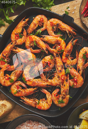 Image of Roasted tiger prawns on iron grilling pan with fresh persley, lemon, chilli and bread