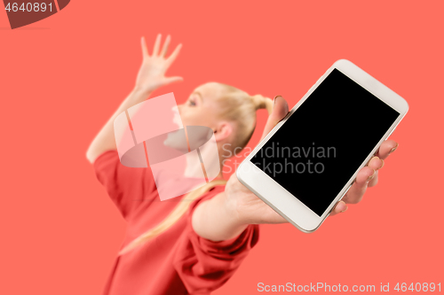 Image of Portrait of a confident casual girl showing blank screen mobile phone isolated over coral background