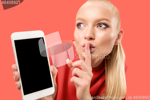 Image of Portrait of a confident casual girl showing blank screen mobile phone isolated over coral background