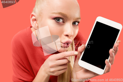 Image of Portrait of a confident casual girl showing blank screen mobile phone isolated over coral background