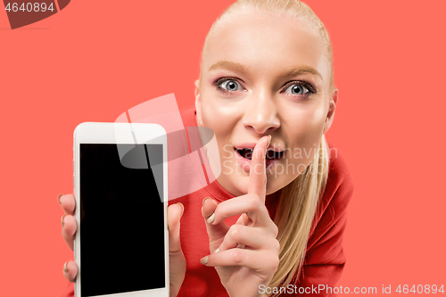 Image of Portrait of a confident casual girl showing blank screen mobile phone isolated over coral background