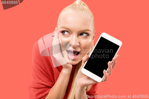 Image of Portrait of a confident casual girl showing blank screen mobile phone isolated over coral background