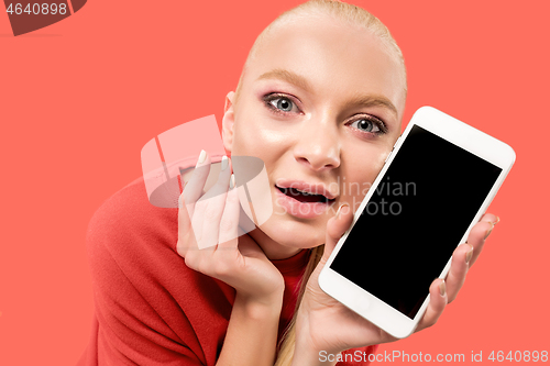 Image of Portrait of a confident casual girl showing blank screen mobile phone isolated over coral background