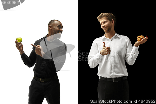 Image of Men eating a hamburger and fruits on a black and white background