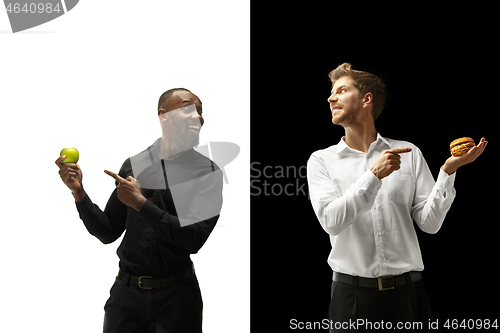 Image of Men eating a hamburger and fruits on a black and white background