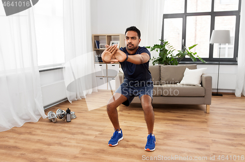 Image of indian man exercising and doing squats at home