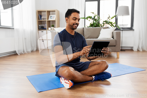 Image of indian man with tablet pc and exercise mat at home