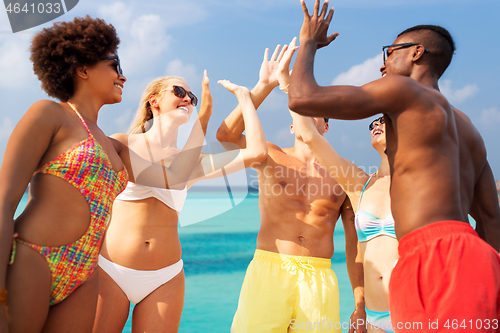 Image of happy friends making high five on summer beach