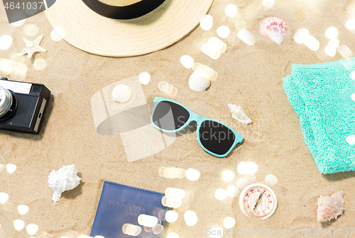 Image of camera, passport, sunglasses and hat on beach sand