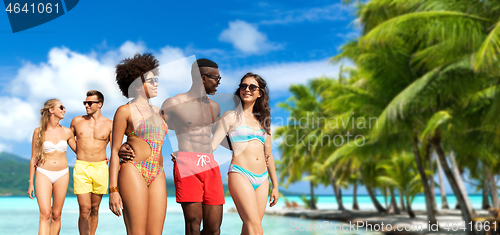 Image of happy friends walking along summer beach