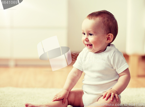 Image of happy baby boy or girl sitting on floor at home