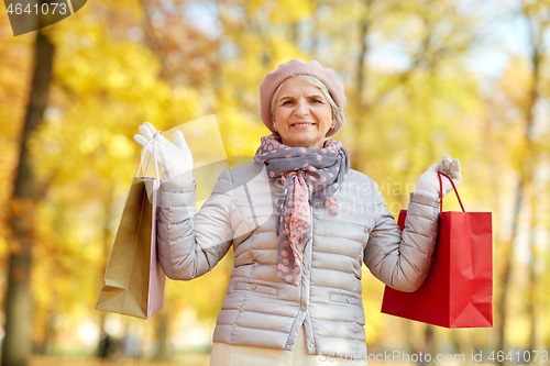 Image of senior woman with shopping bags at autumn park