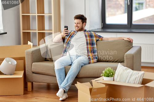 Image of man with smartphone and boxes on sofa at new home