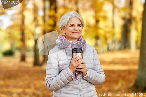 Image of old woman with hot drink in tumbler at autumn park