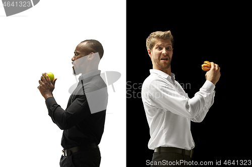 Image of Men eating a hamburger and fruits on a black and white background