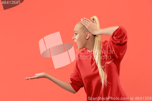 Image of Beautiful female half-length portrait isolated on coral studio backgroud. The young emotional surprised woman