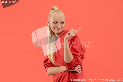 Image of The young woman whispering a secret behind her hand over coral background