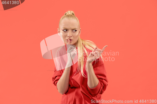 Image of The young woman whispering a secret behind her hand over coral background