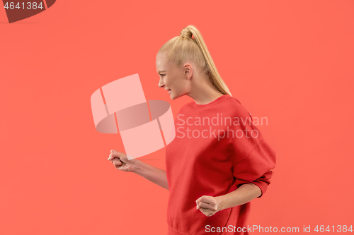 Image of Beautiful female half-length portrait isolated on coral studio backgroud. The young emotional surprised woman